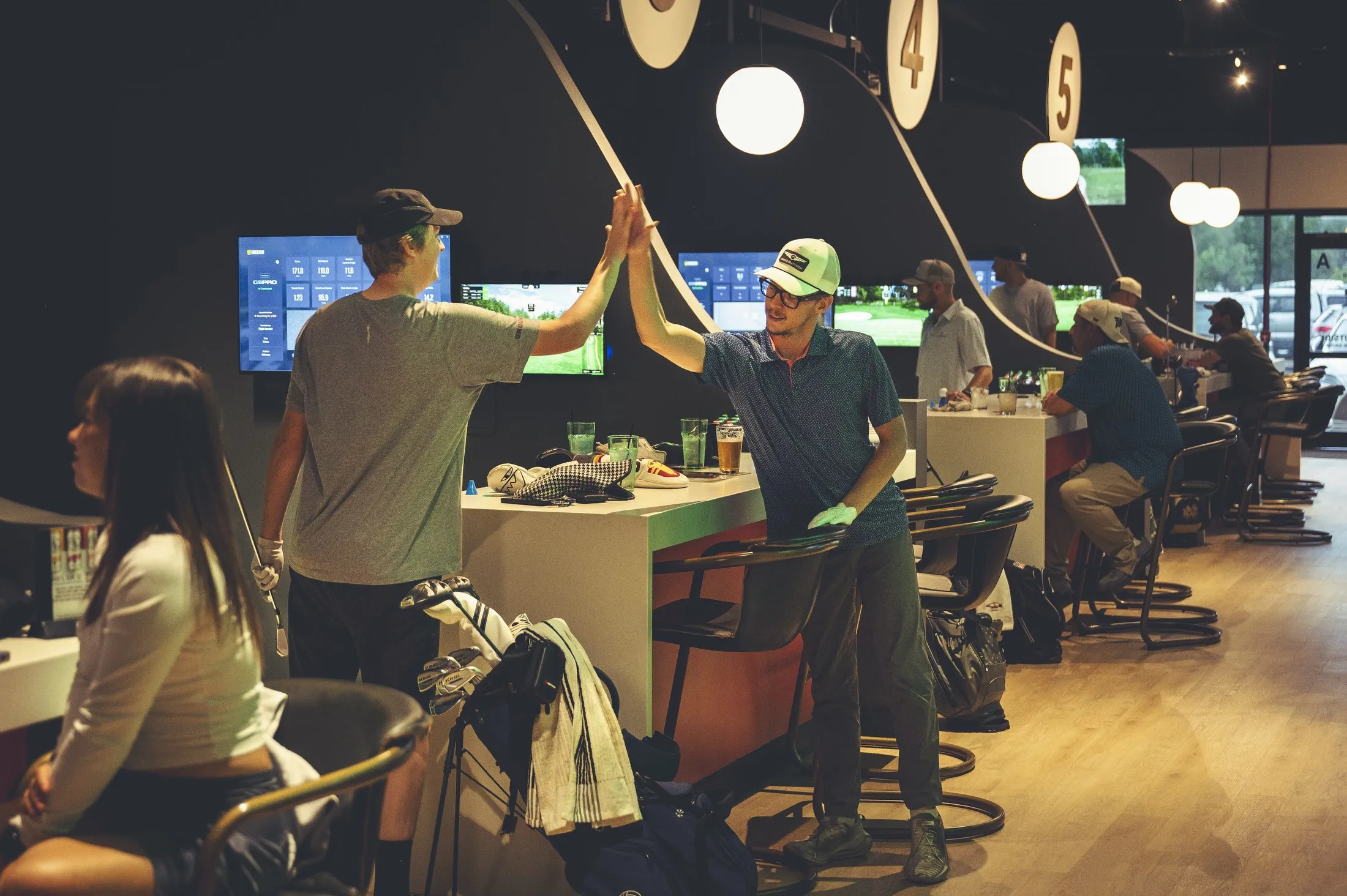 Friends high-fiving between golf simulator bays at The PAR Club