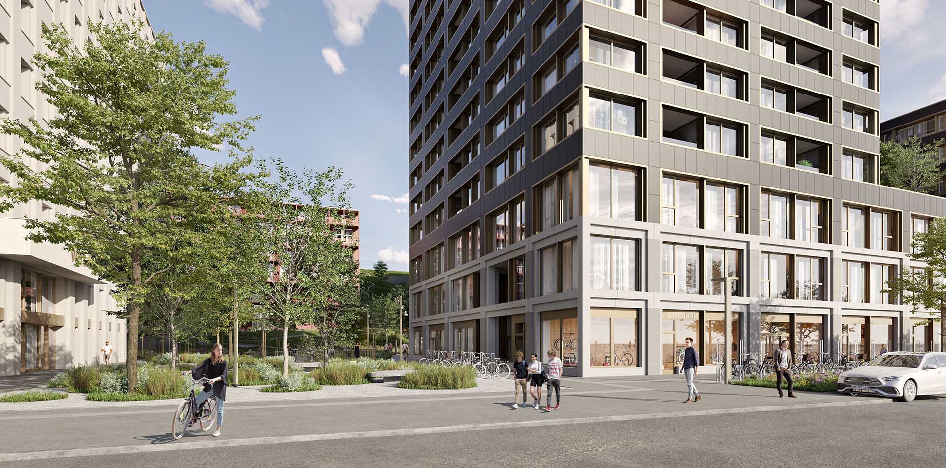 Modern urban street scene with a large multi-story building featuring many windows and a bike shop on the ground floor, people walking and a person pushing a bicycle, surrounded by green trees and landscaping under a partly cloudy sky.