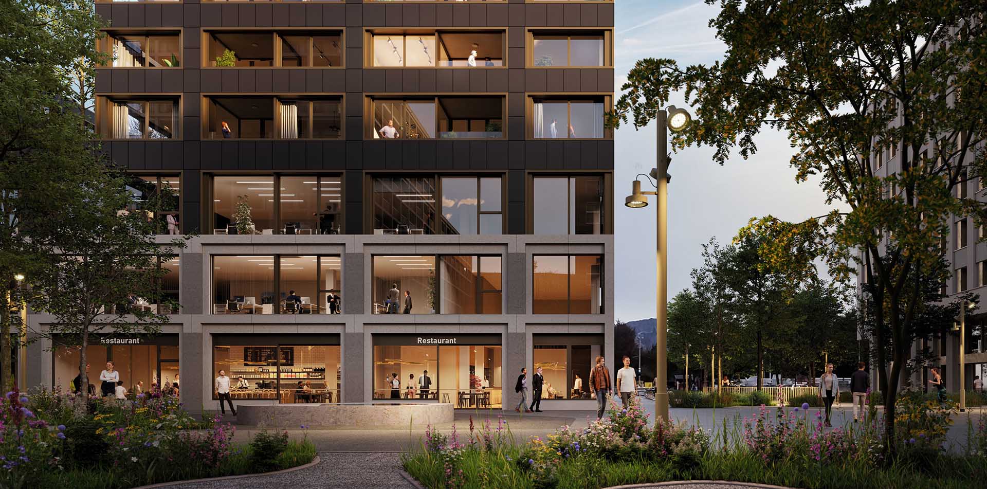 Modern multi-story building with large windows, ground floor restaurant with people inside and walking outside in a plaza surrounded by trees and flower beds at dusk.