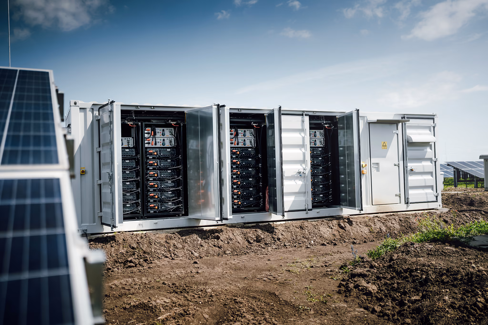 Otevřené kontejnerové bateriové úložiště s bateriovými moduly vedle fotovoltaických panelů