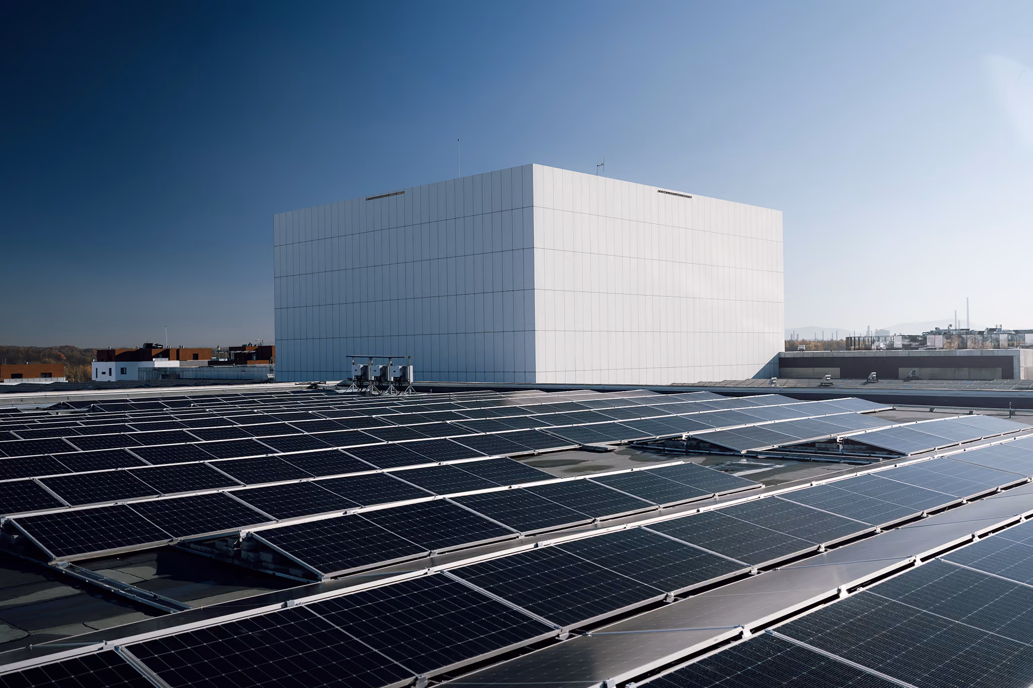 Střešní fotovoltaická elektrárna před bílou technologickou budovou