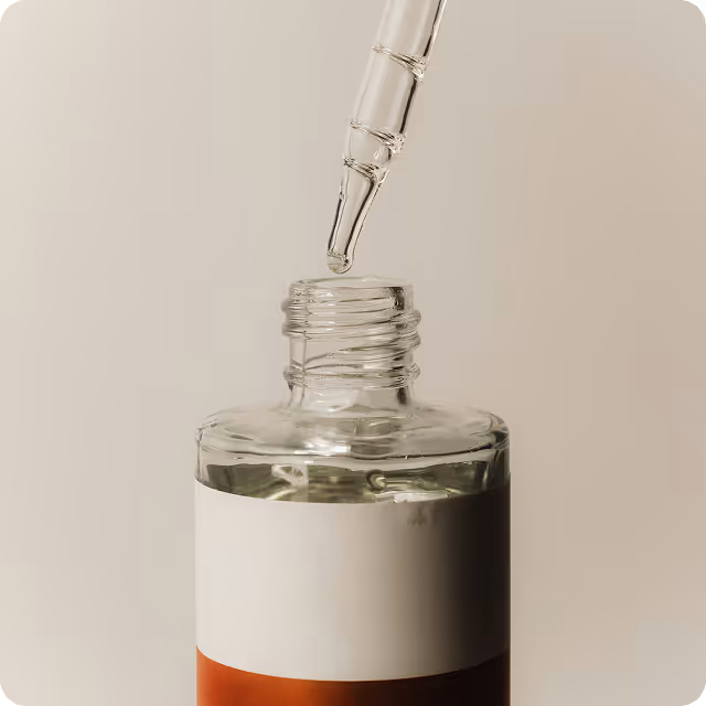 Close-up of a dropper dispensing liquid into an open glass bottle with a two-tone label.