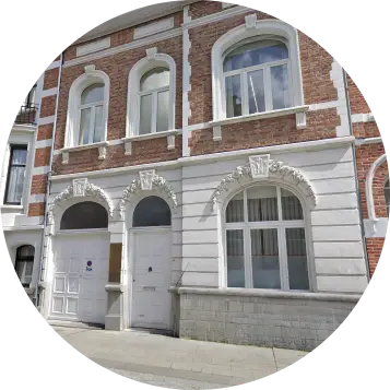Facade of a historic brick and stone building with white decorative arches above windows and doors on the ground floor and arched windows on the upper floor.