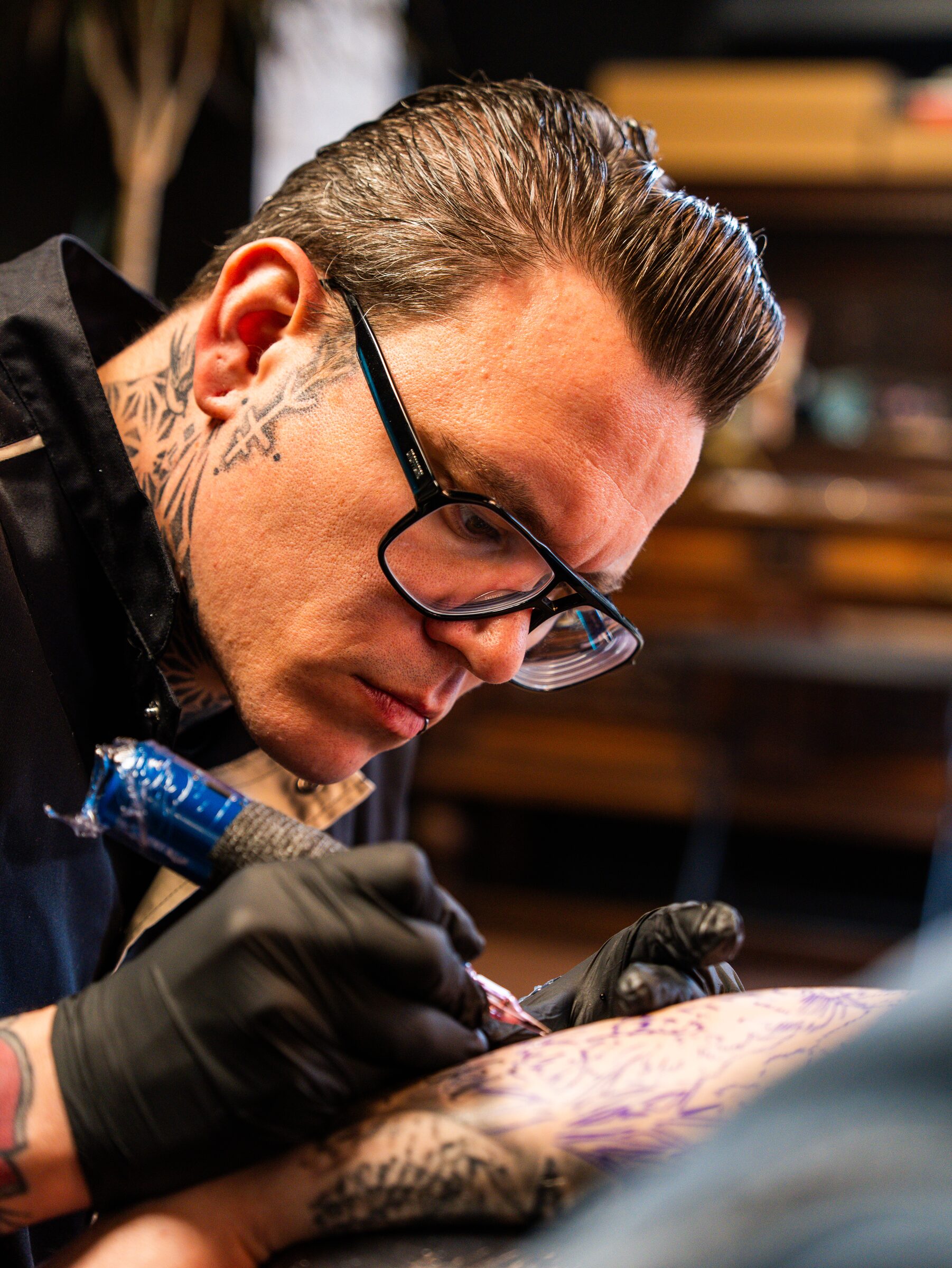 Tattooartiest met bril werkt geconcentreerd aan een tatoeage bij InkHeaven in Emmen