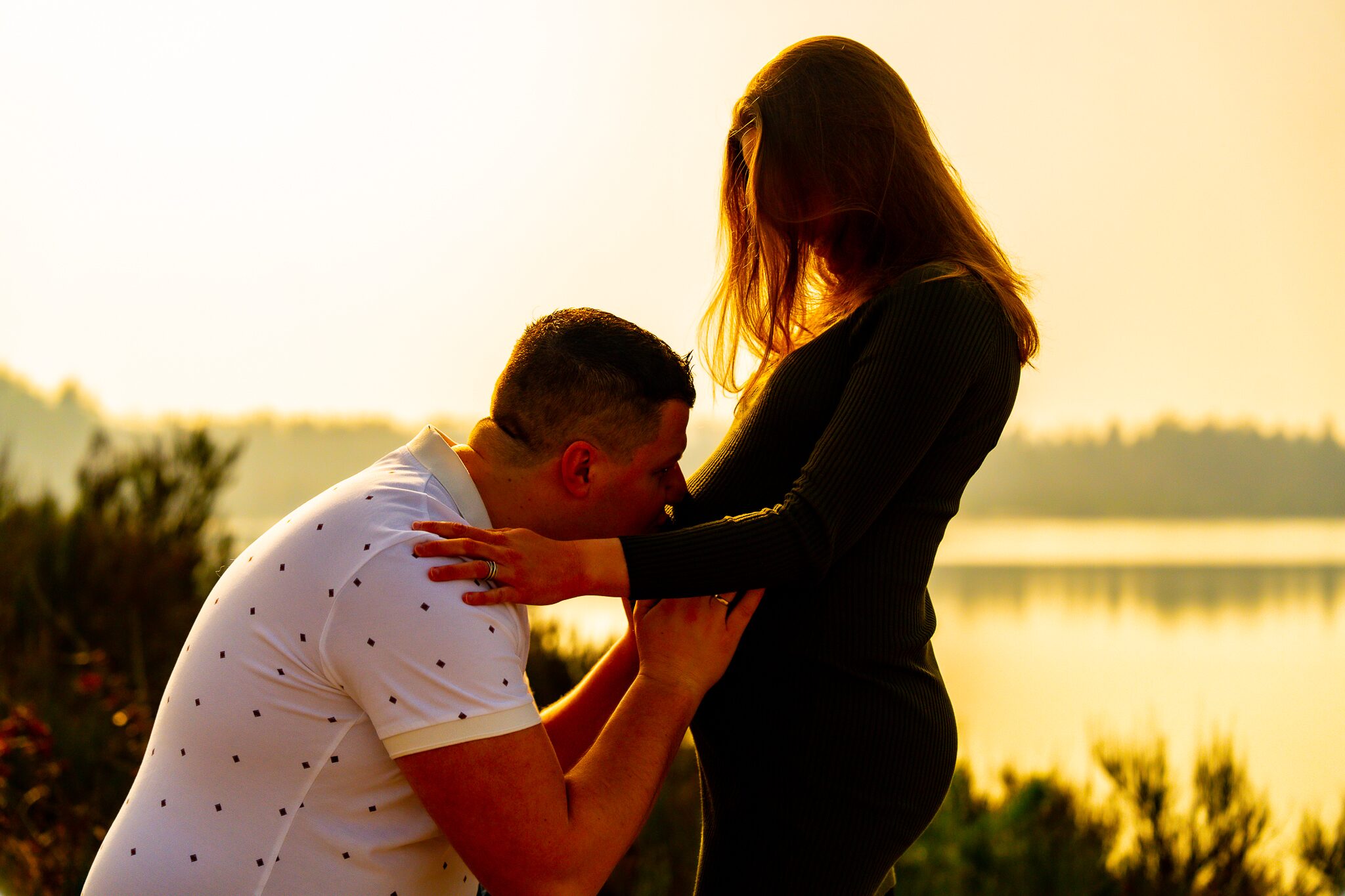 Partner kust de zwangere buik tijdens een shoot bij zonsondergang