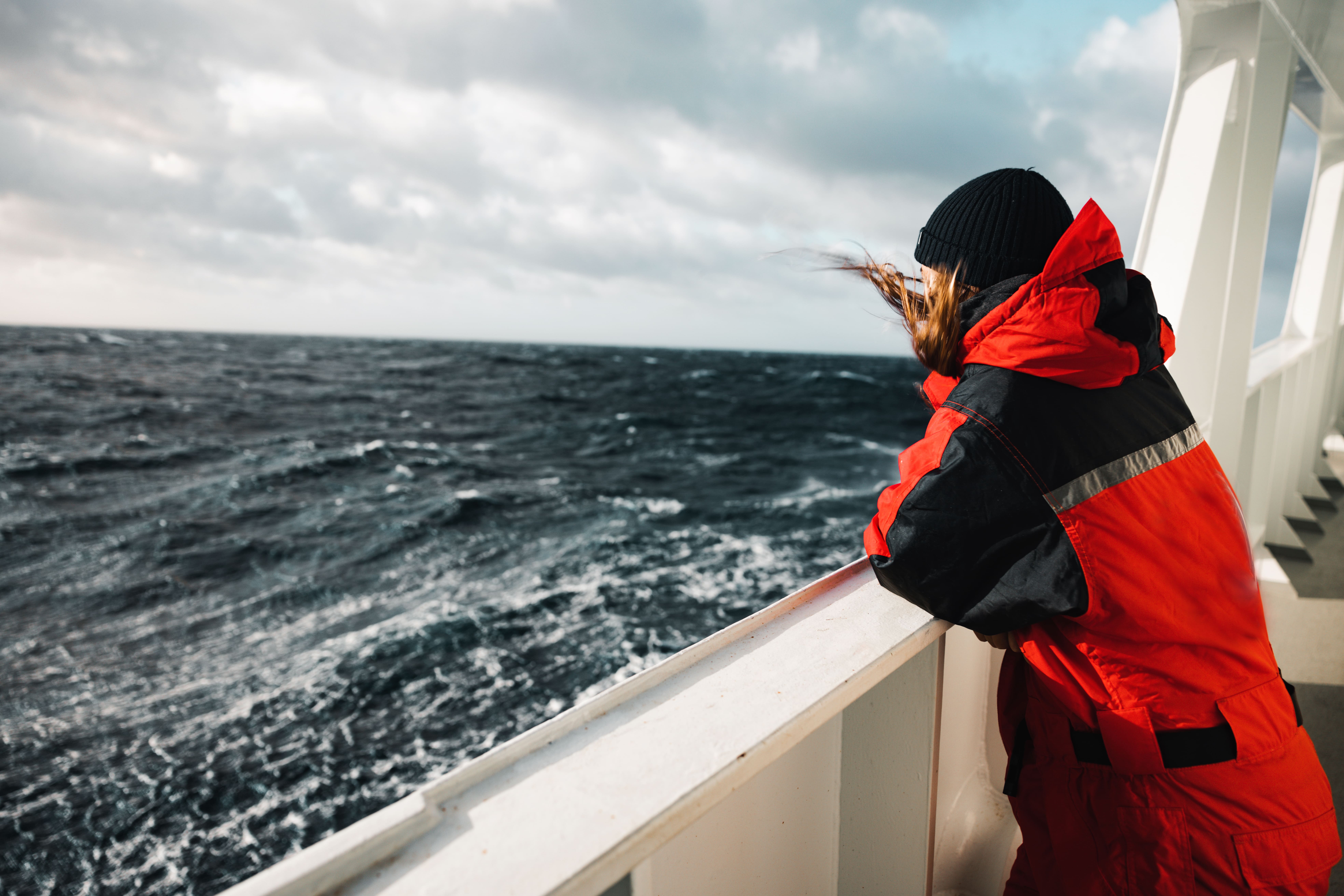 Person in red survival suit looking over rough ocean from a ship, symbolizing HELINOR Energy’s mission to deliver reliable, zero-emission power in harsh maritime environments