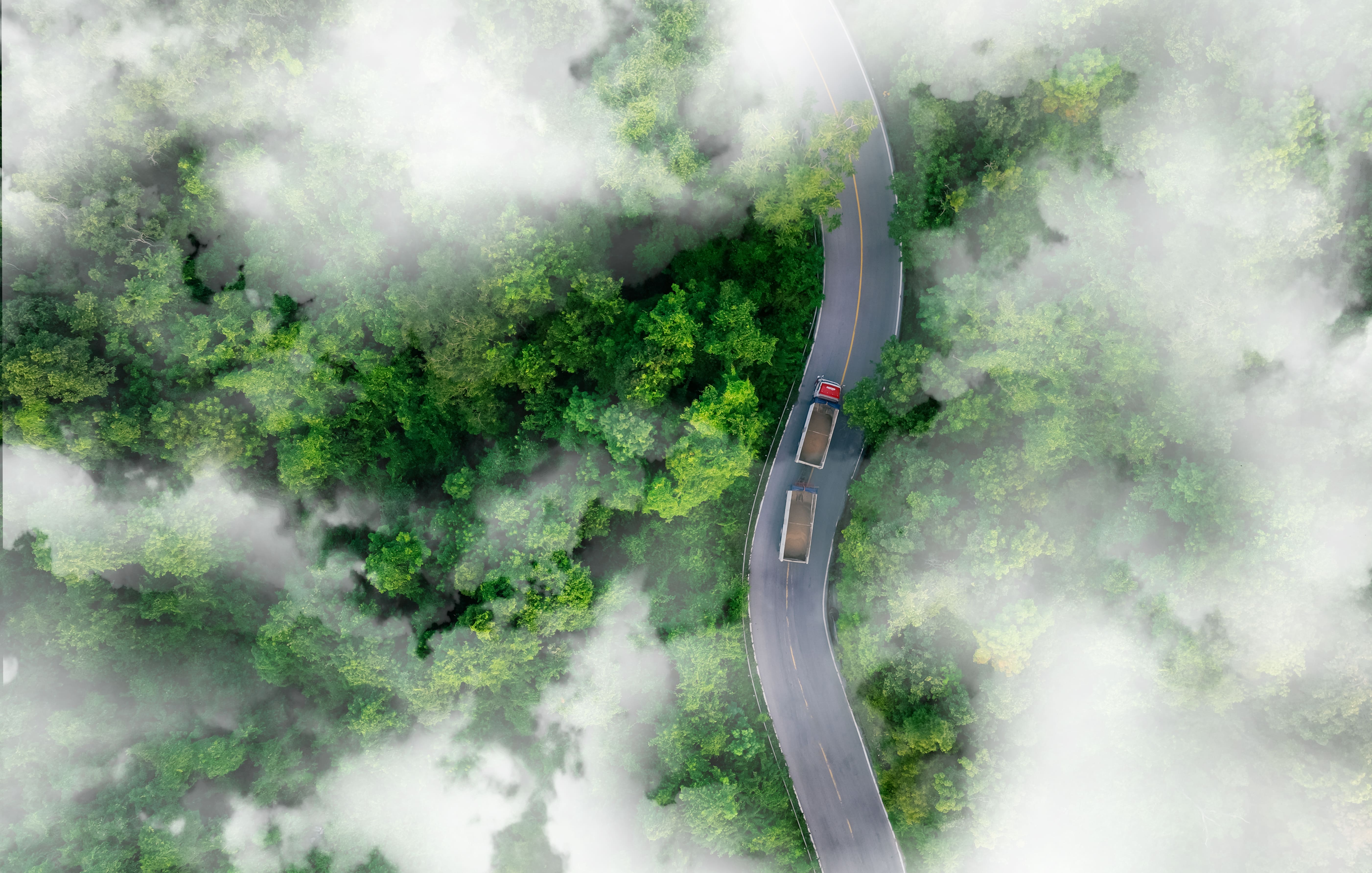 Aerial view of hydrogen-powered trucks driving through a green forest with fog, symbolizing HELINOR Energy’s vision for a clean, sustainable, zero-emission future