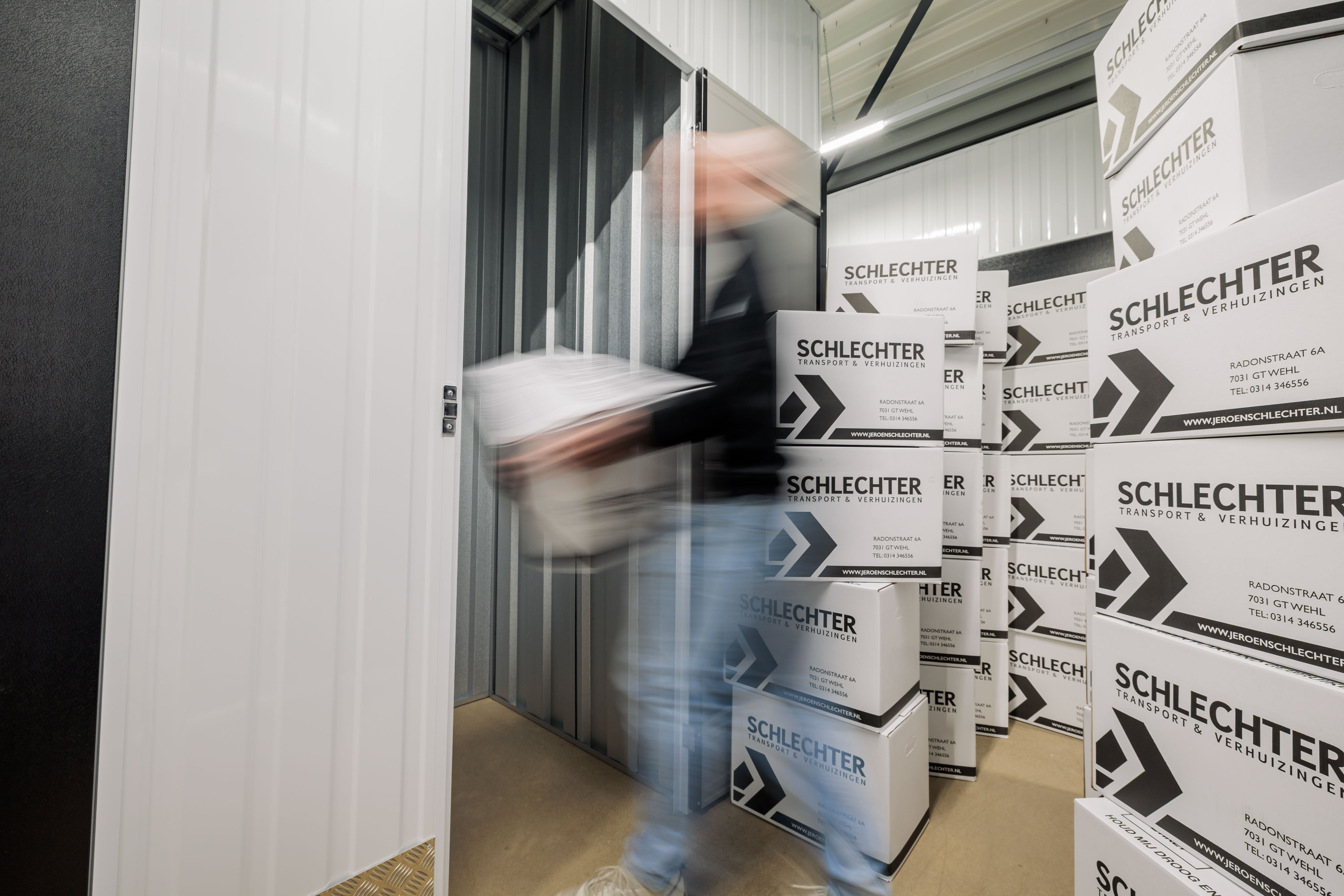 Medewerker draagt dozen een opslagruimte in, met gestapelde verhuisdozen op de voorgrond