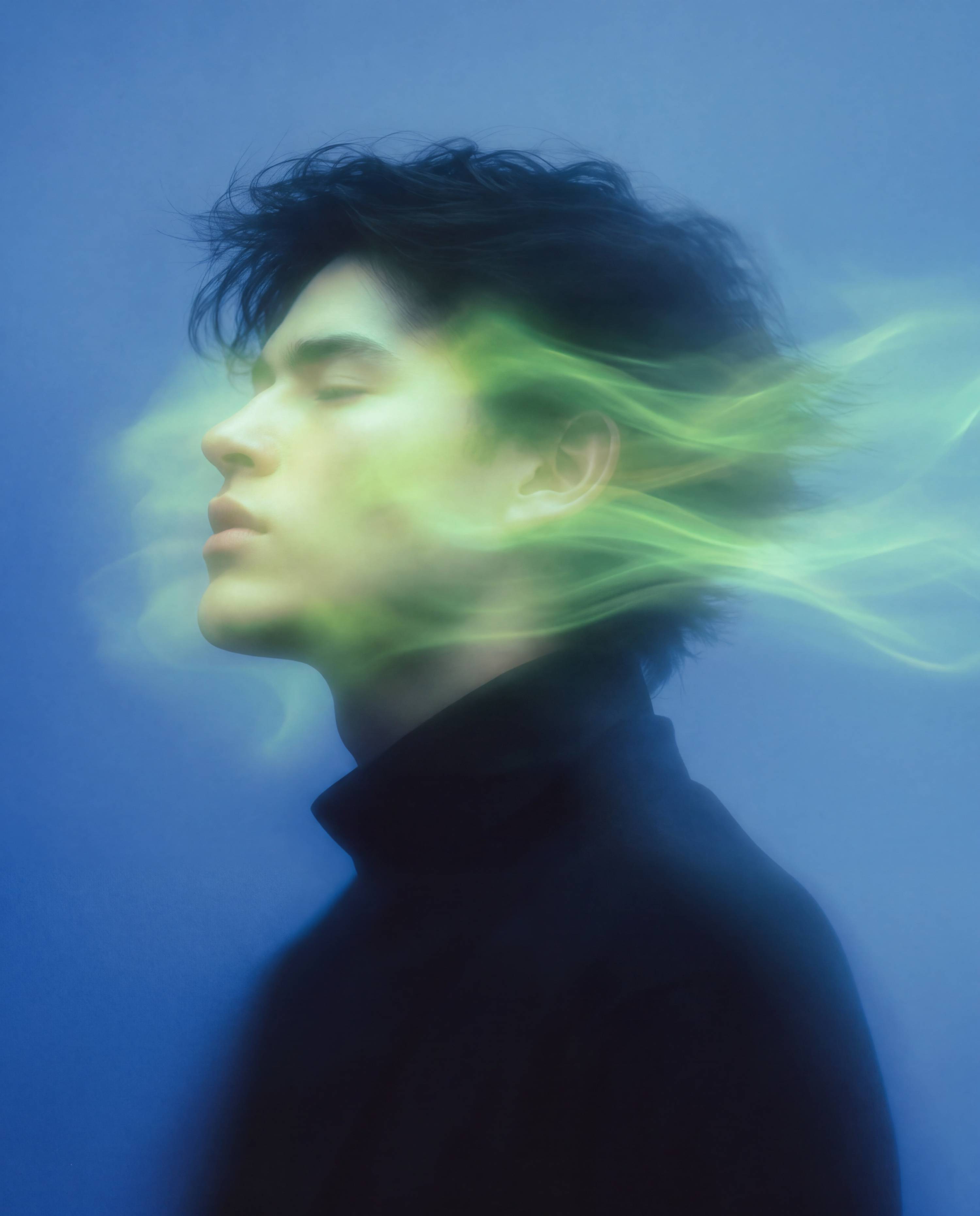 Man in profile with green smoke streaming past his face against a blue background