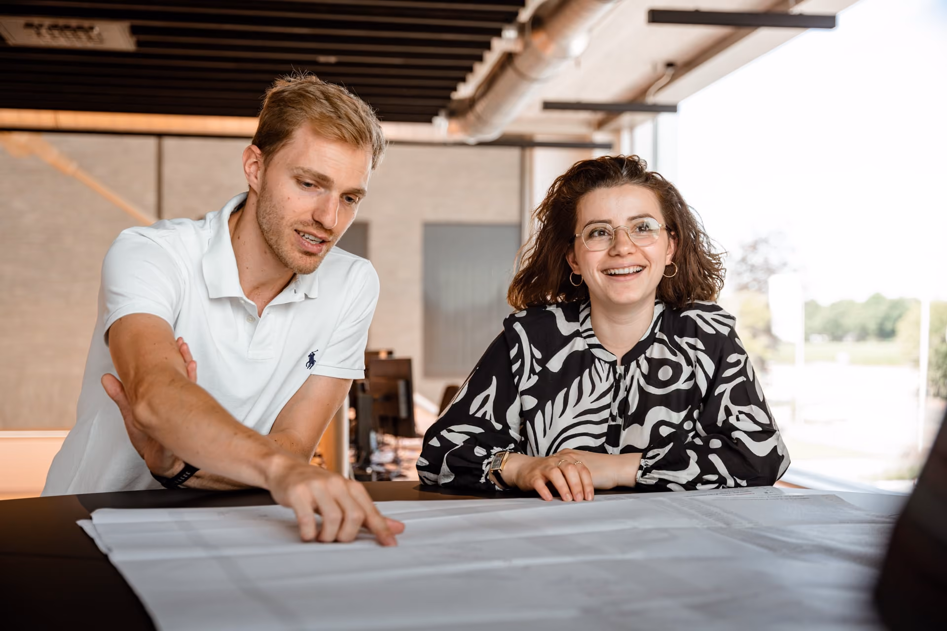 A facade engineer and a client representative studying a large technical drawing spread out on a table.
