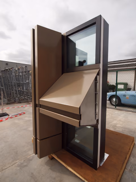 Full-size bronze-framed unitised facade mock-up standing outdoors on a pallet for inspection.