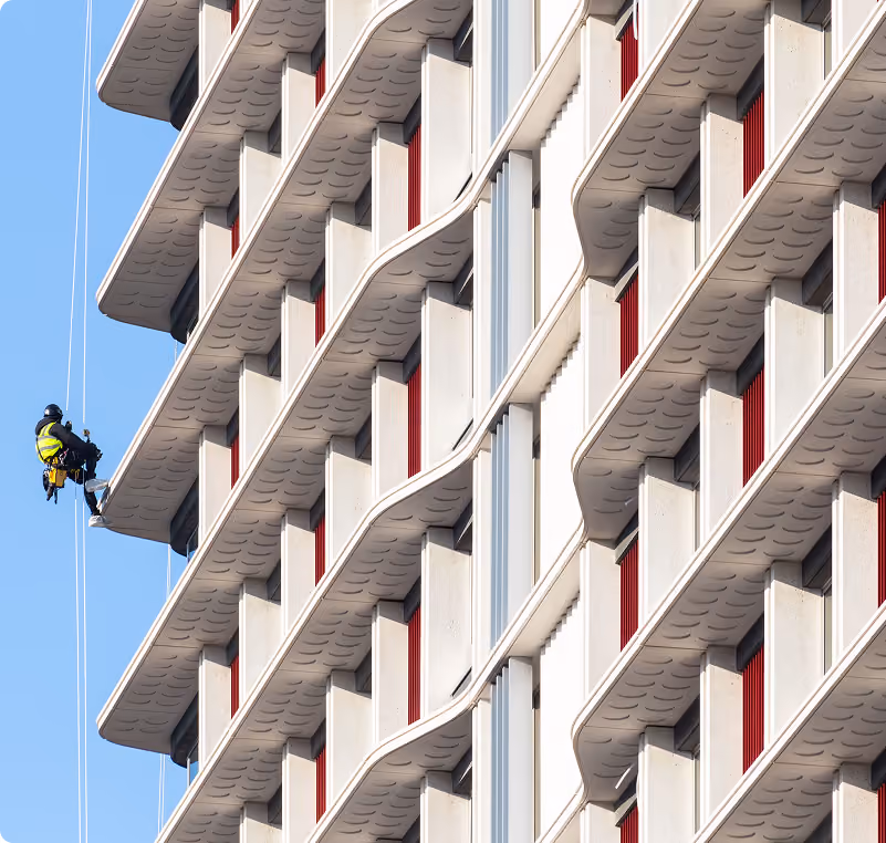 Rope access technician abseiling down a residential facade with angled precast balconies.