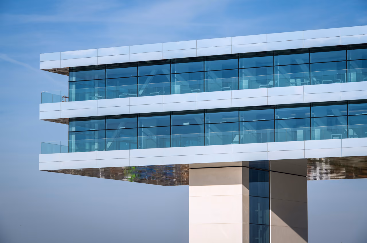 The Cordeel office building, a glazed volume cantilevered over a solid base against a clear sky.