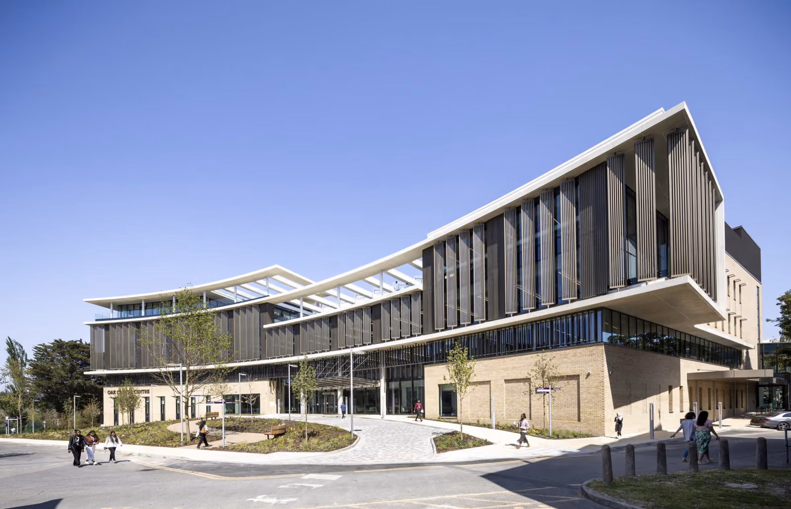 The Oak Cancer Centre with its sweeping curved roof and timber louvred facade above a paved forecourt.
