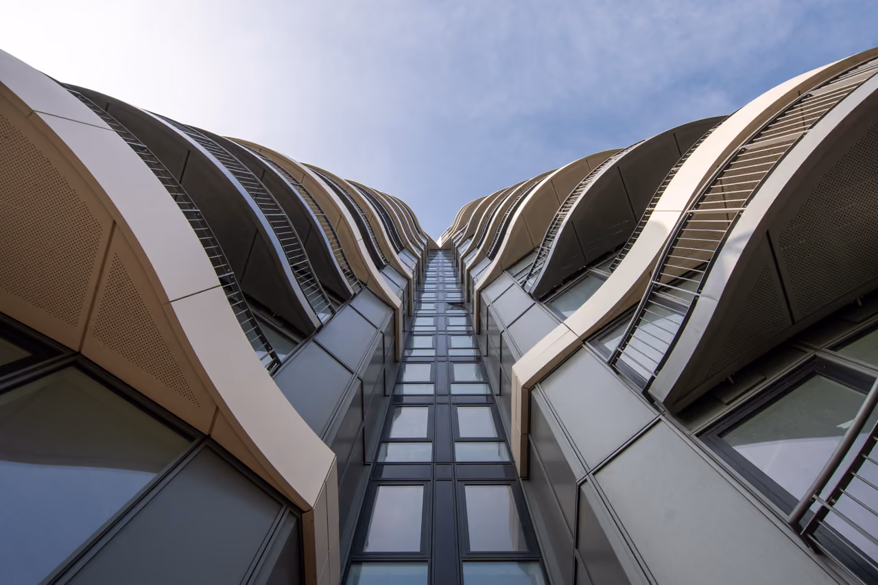 View looking up at a modern high-rise building with curved balconies and glass windows against a partly cloudy sky.