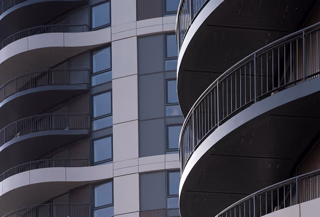 Close-up view of modern building facades featuring curved balconies with metal railings and large rectangular windows.