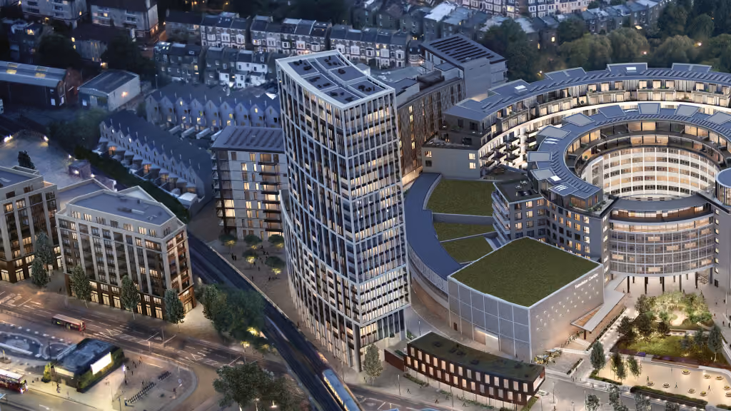 Aerial nighttime view of a modern urban area featuring a tall rectangular glass skyscraper and a large circular building with a central open courtyard, surrounded by smaller buildings and residential houses in the background.