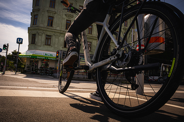 Low-angle photograph of a cyclist riding through a city street.