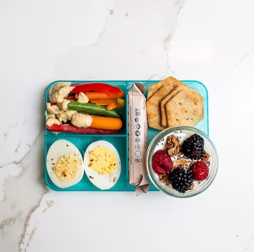 Gut-friendly healthy bento box lunch for kids with vegetables, hummus, boiled eggs, berries, yogurt, and crackers