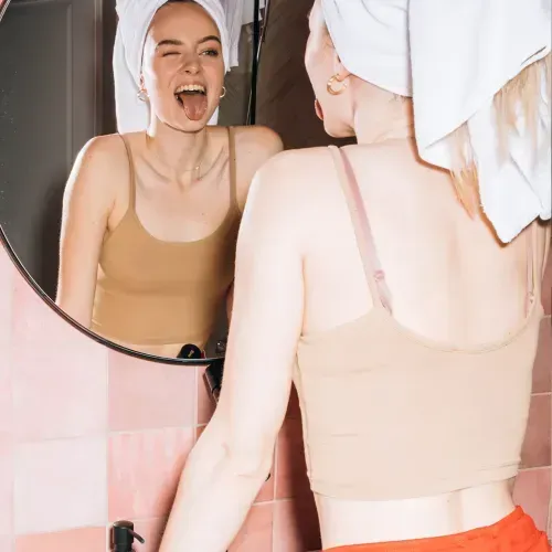 A young woman with her hair wrapped in a towel, sticking her tongue out at her reflection in a mirror