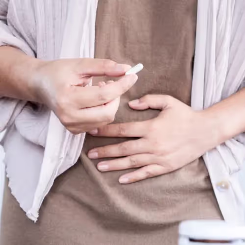 A woman holds her stomach and holds a probiotic pill to help with bloating
