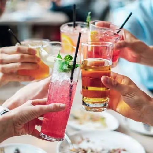 Hands toasting with various alcoholic beverages at a gathering, highlighting concerns about alcohol's impact on gut health