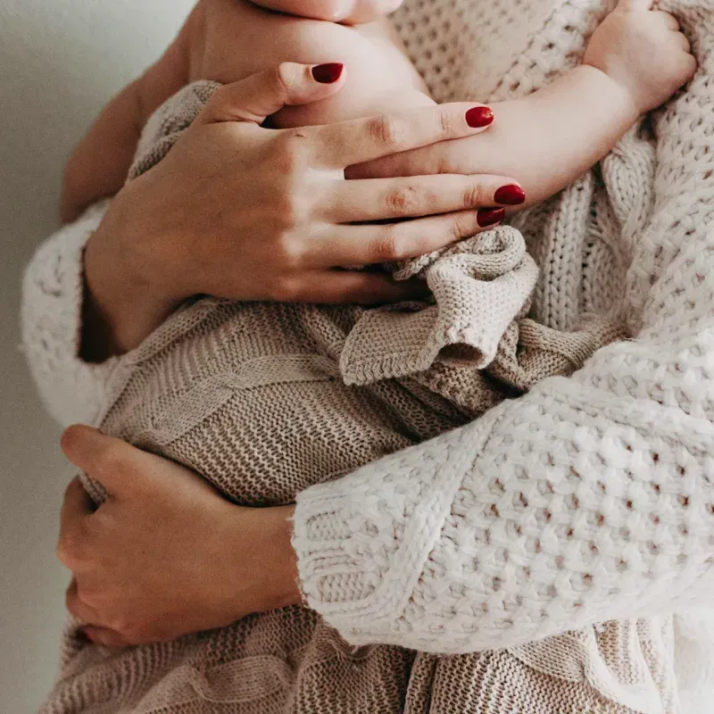 A mother gently holds her baby, wrapped in a cozy, textured blanket