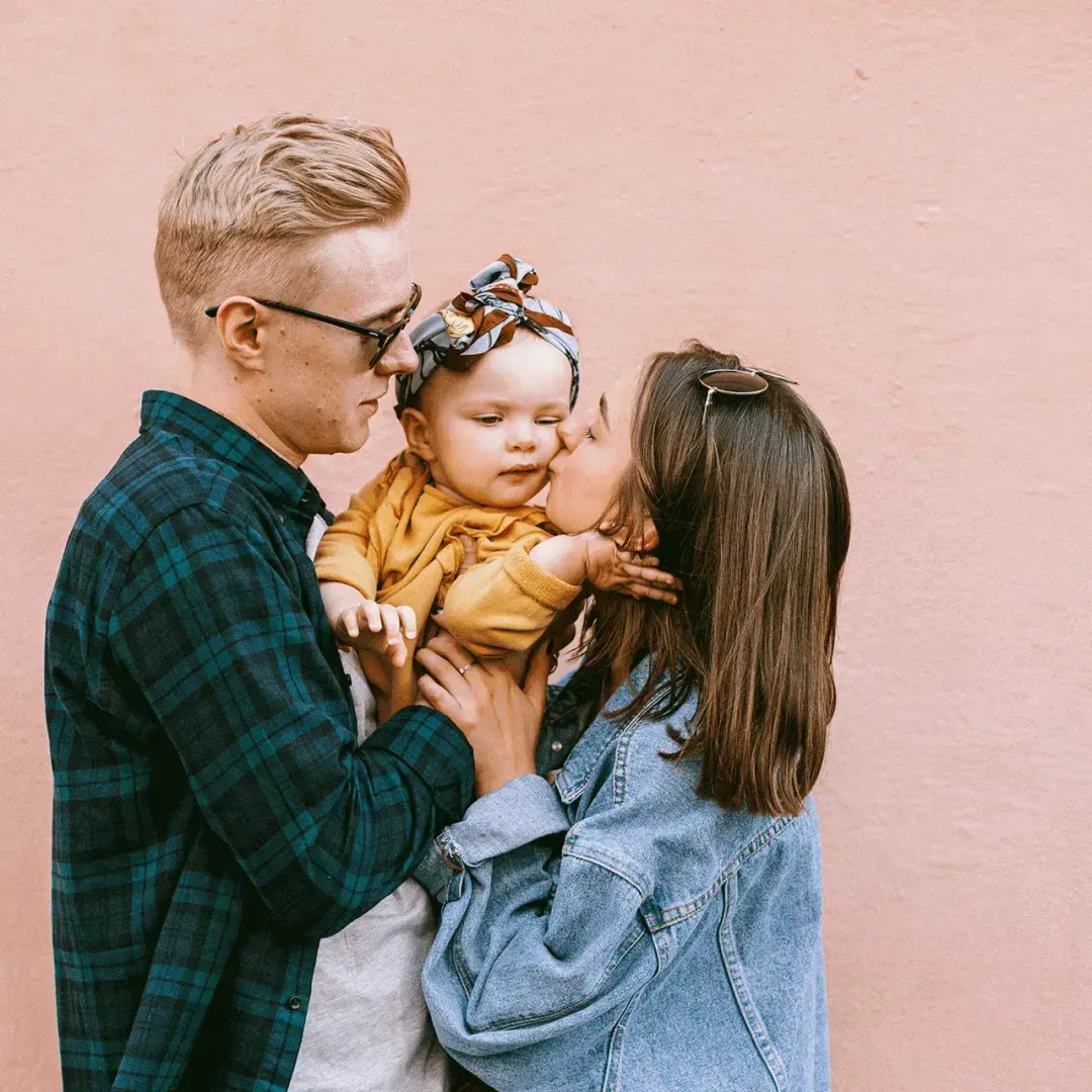 Parents affectionately kissing their baby, representing a family managing atopic march conditions together