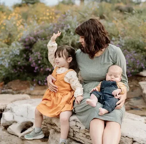 Mother sitting outdoors with her two young children, reflecting on how their births affected their gut microbiomes