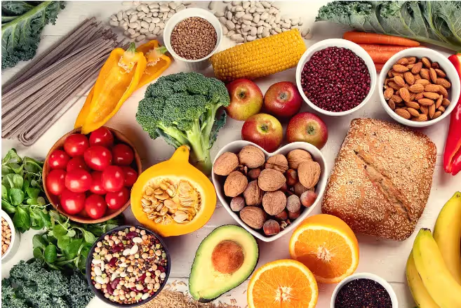 A colorful assortment of fresh fruits, vegetables, nuts, and grains displayed on a white surface.