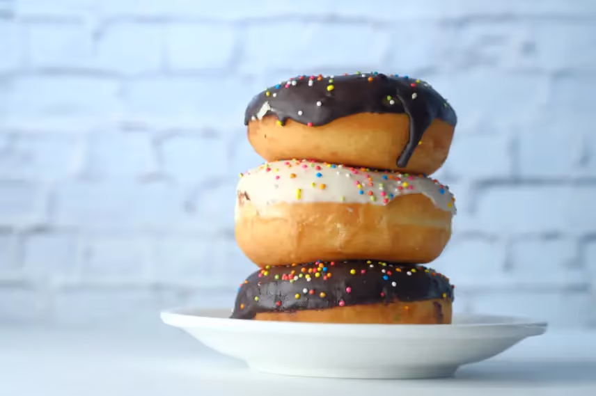 A stack of three donuts with chocolate and white icing, topped with colorful sprinkles, on a white plate.