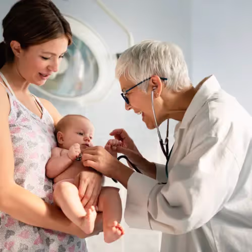A pediatrician provides preventative care to a young baby in the arms of its mother