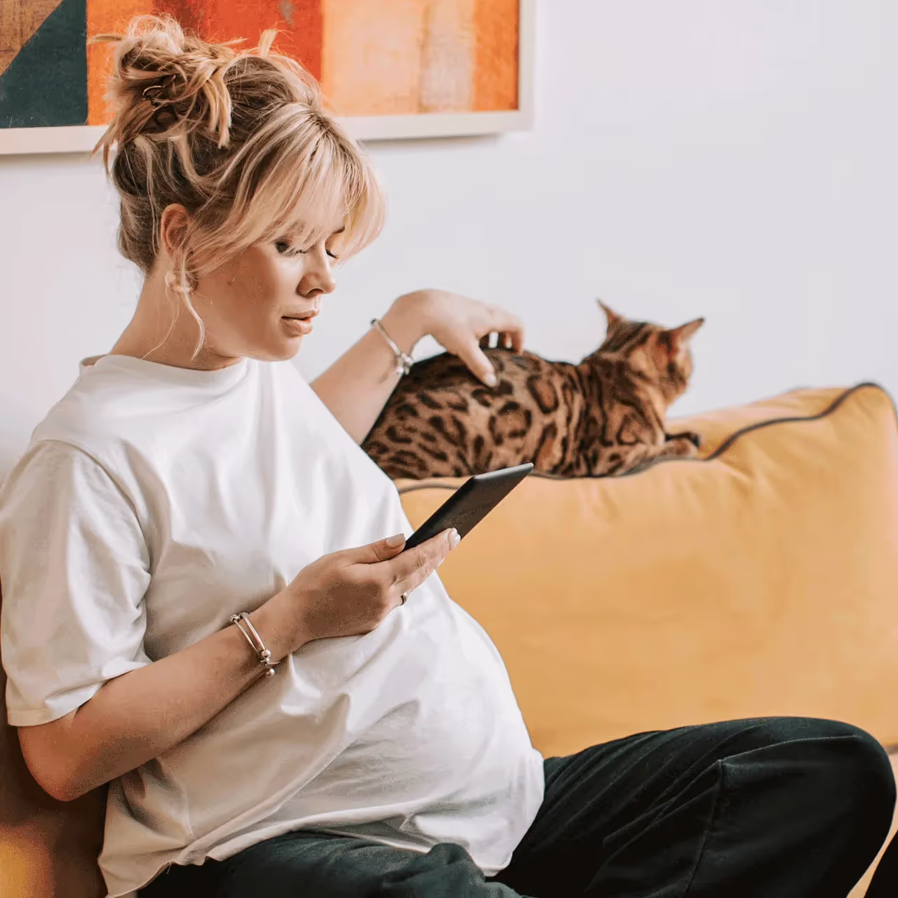 Pregnant woman reading about a gut-friendly birth plan while petting her cat on the couch