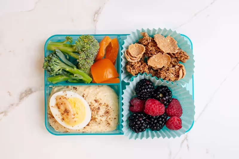 A rainbow-inspired bento box lunch with veggies, hummus, berries, granola, and a hard-boiled egg with miso, all package-free
