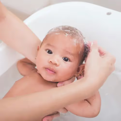 A mother gently shampoos her baby's scalp during bath time to care for cradle cap