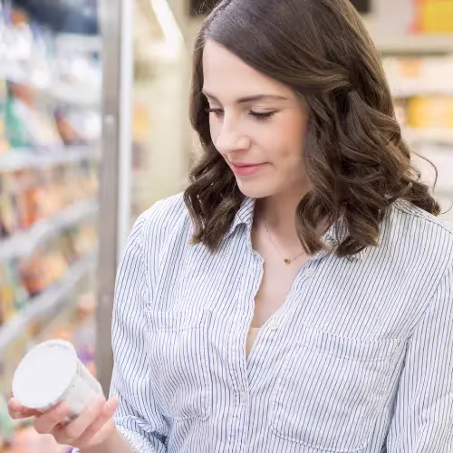 A woman checks the nutritional label on a product at the store in a grocery aisle.