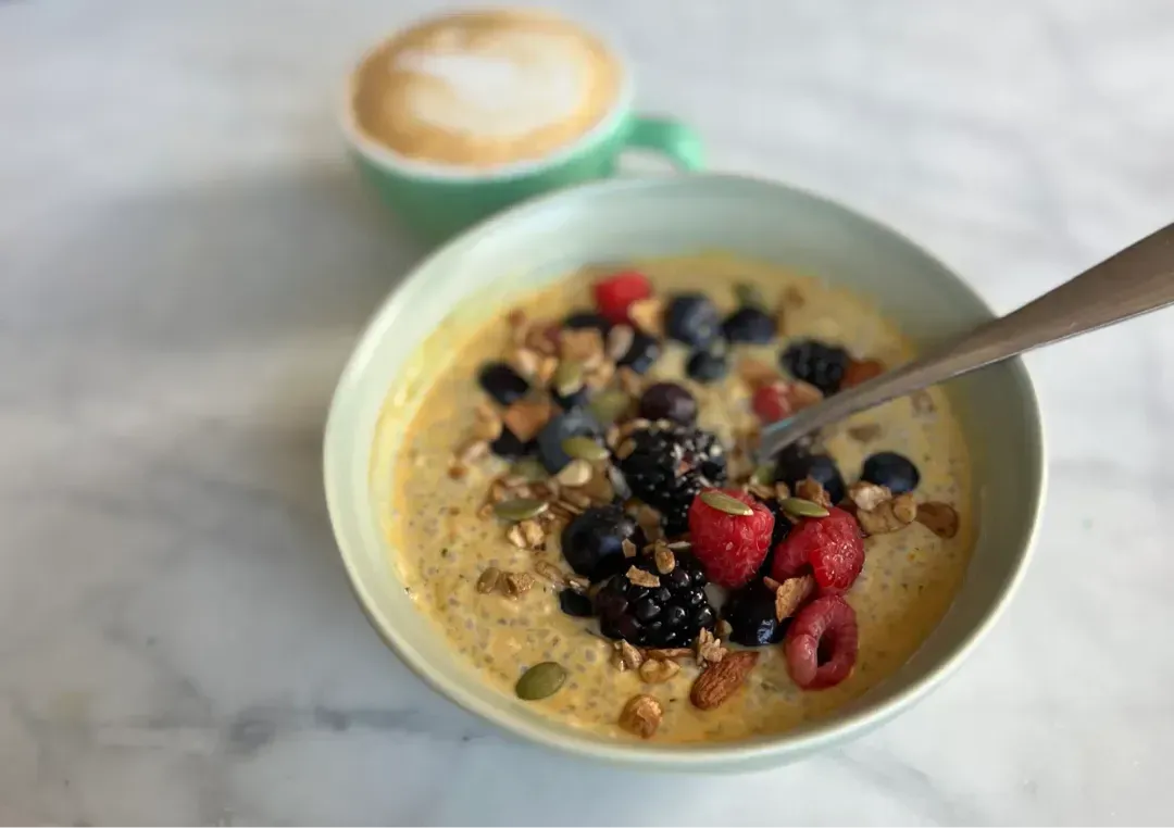 A bowl of chia pudding with berries and granola next to a latte