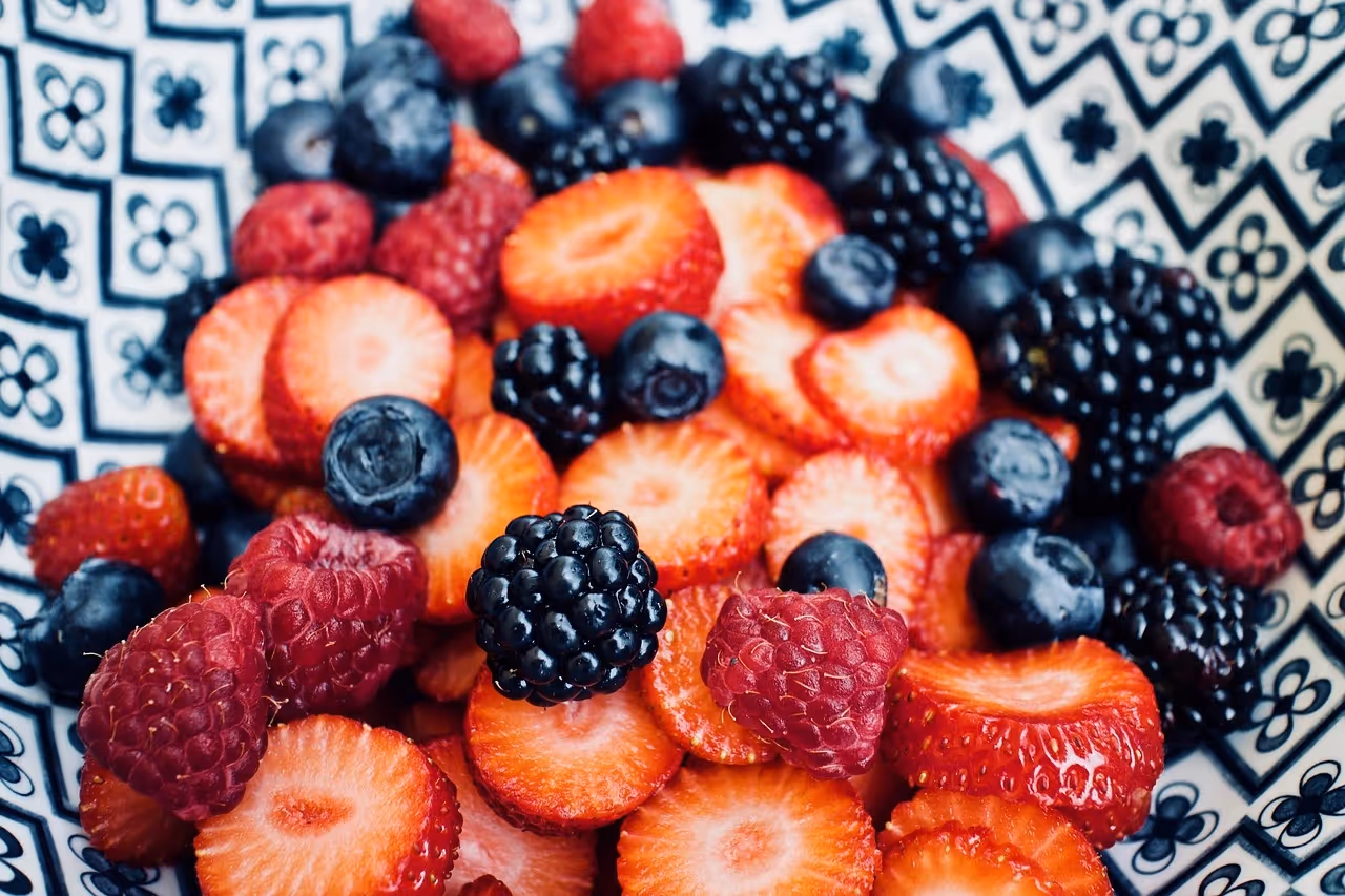 A close-up bowl of mixed berries including sliced strawberries, raspberries, blueberries, and blackberries, served in a patterned dish.