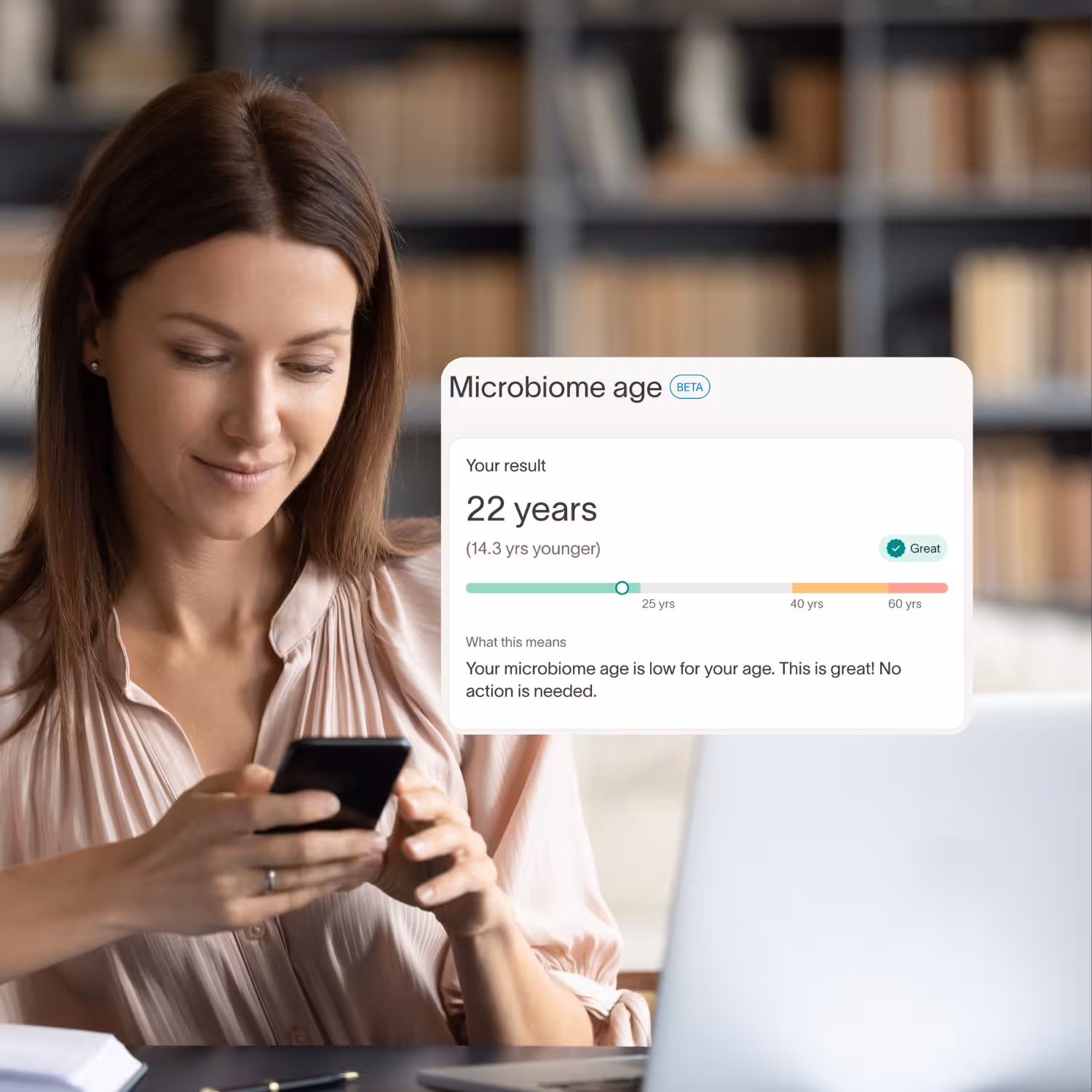 Woman smiling at her phone beside laptop, with a Tiny Health Microbiome age card showing 22 years, 14.3 years younger, Great.