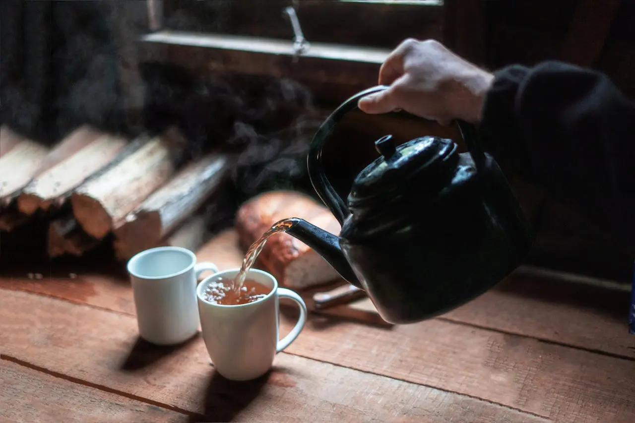 Pouring steaming tea into white mugs, with a cozy cabin vibe and firewood stacked nearby.