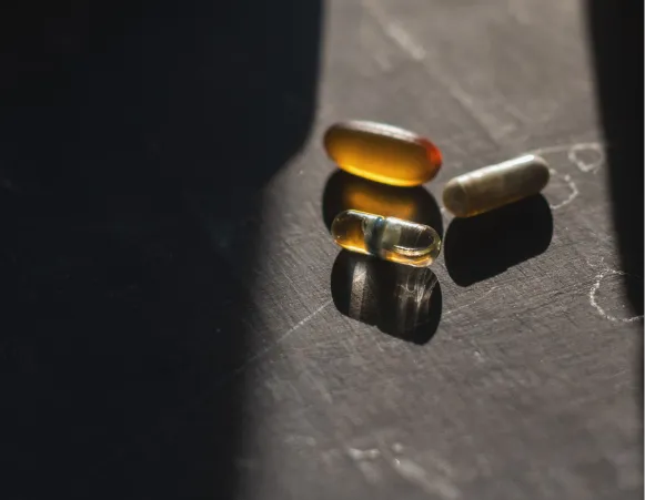 Three capsules of different colors and shapes are resting on a surface, reflecting light.