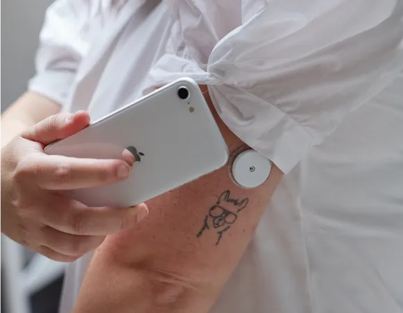 a person reading a glucose monitor from their arm using a smartphone 