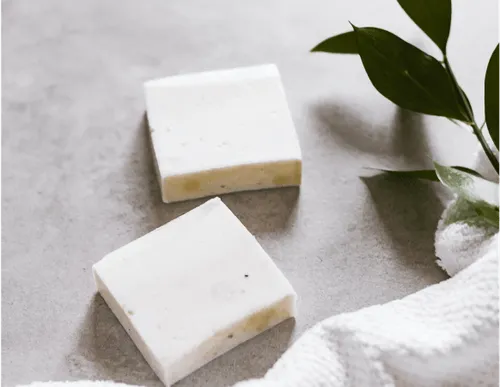 two bars of soap close to a towel and a  plant branch 