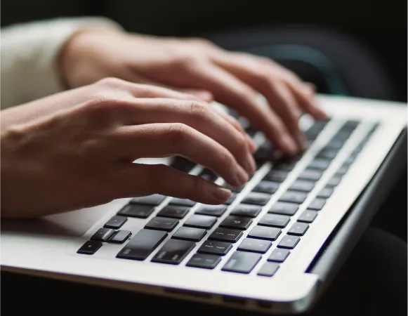 Close-up of hands typing on a laptop keyboard, with fingers positioned over the keys.