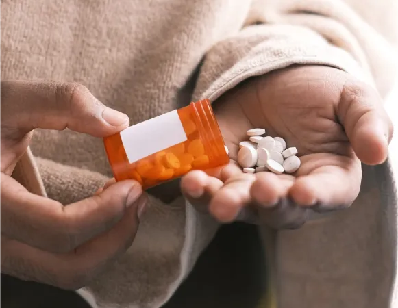 A hand holds an orange prescription bottle while the other hand catches white pills spilling out.