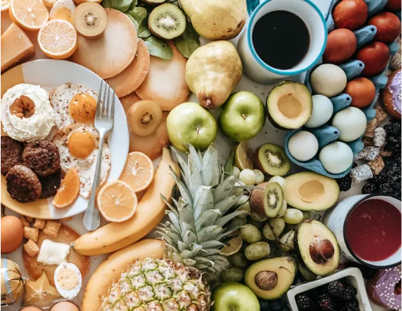 A vibrant spread of various fruits and breakfast items, including eggs, sausage, and pancakes, arranged on a table with coffee and colorful dishes.