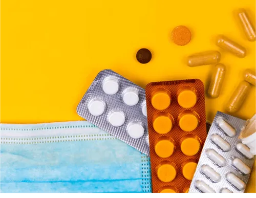 A flat lay of various medications, including blister packs and loose pills, alongside a blue medical mask.