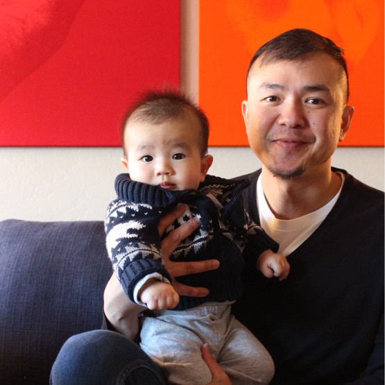 A happy father of asian features smiling to camera with his baby in arms