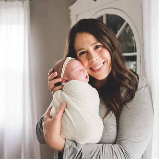 A happy mother of caucasian features and brown hair in her home with her baby in arms