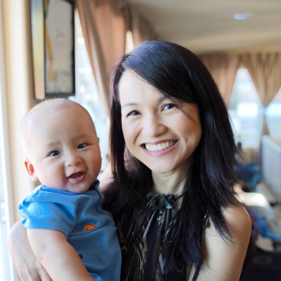 A happy mother of asian features and black hair in her home with her baby in arms
